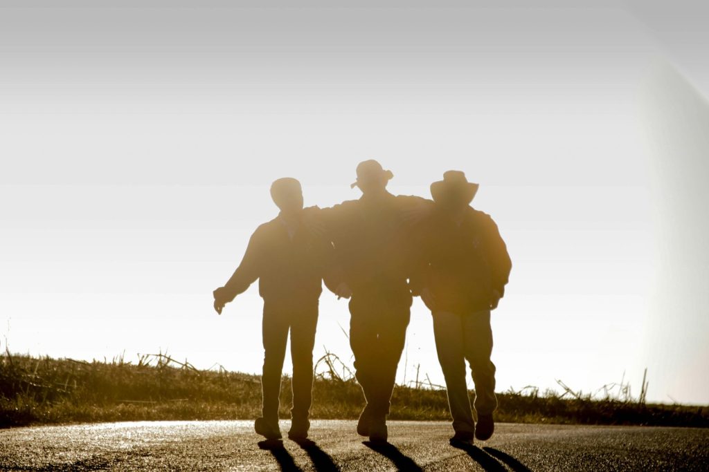 Three friends walk arm in arm along a country road at sunset, capturing a moment of unity.